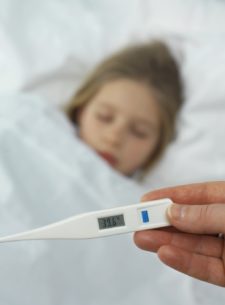 Little girl in bed sick, adult holding thermometer in hand